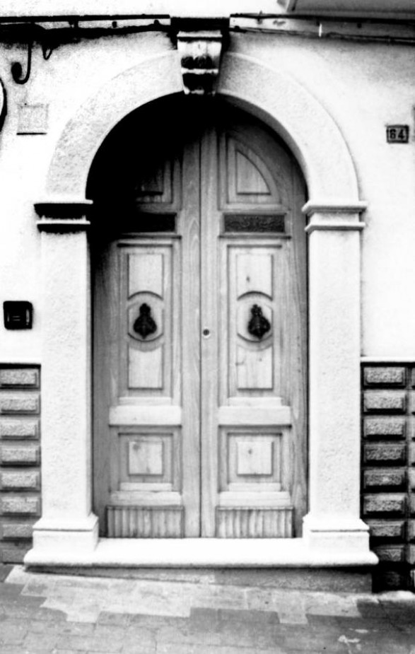 Fig. 34 Corso Matteotti 66. Portale ad arco a tutto sesto con stemma in chiave d'arco a protiride, decorato con figure a bassorilievo e con motivi floreali; poggia su imposte dei piedritti a capitello e basi rimarcate; è una copia identica di quello preesistente, sostituito di recente in seguito alla ristrutturazione dell'edificio. Particolare: Stemma in chiave d'arco a protiride, decorato con elementi a bassorilievo. Fig. 34 Corso Matteotti 66. Portale ad arco a tutto sesto con stemma in chiave d'arco a protiride, decorato con figure a bassorilievo e con motivi floreali; poggia su imposte dei piedritti a capitello e basi rimarcate; è una copia identica di quello preesistente, sostituito di recente in seguito alla ristrutturazione dell'edificio. Particolare: Stemma in chiave d'arco a protiride, decorato con elementi a bassorilievo.