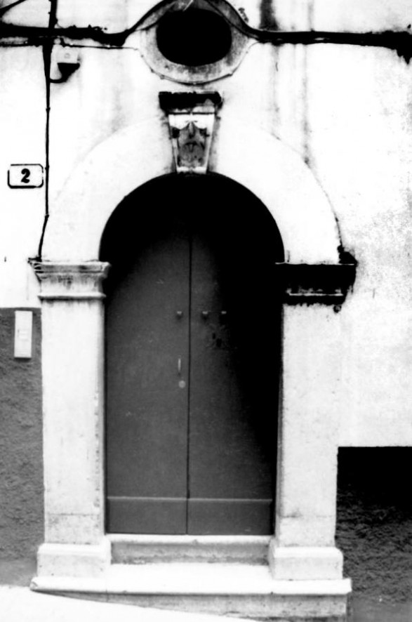 Fig. 35 Via Custoza 2. Portale ad arco a tutto sesto con stemma in chiave d'arco a protiride decorato con elementi a bassorilievo; con imposte dei piedritti a capitello e basi rimarcate ed è sovrastato da una finestrella di forma circolare. Particolare: Stemma in chiave d'arco a protiride con decorazioni a bassorilievo. Fig. 35 Via Custoza 2. Portale ad arco a tutto sesto con stemma in chiave d'arco a protiride decorato con elementi a bassorilievo; con imposte dei piedritti a capitello e basi rimarcate ed è sovrastato da una finestrella di forma circolare. Particolare: Stemma in chiave d'arco a protiride con decorazioni a bassorilievo.