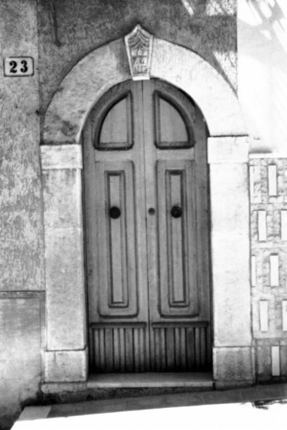 Fig. 40 Via Turati 23. Portale ad arco a tutto sesto con stemma in chiave d'arco di forma pentagonale con iscrizione, poggiante su imposte dei piedritti con basi leggermente rimarcate. Particolare: Stemma in chiave d'arco di forma pentagonale con iscrizione su due righe: 'P.G. 1883'.