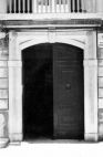 Fig. 14 Corso Matteotti 142. Ampio portale ad arco ribassato, inquadrato, con stemma in chiave d'arco contenente una figura stilizzata a bassorilievo, con imposte dei piedritti e basi rimarcate; con ferma-porta in metallo di forma triangolare (vedi Glossario). Particolare: Stemma in chiave d'arco contenente a bassorilievo una figura stilizzata d' aquila con serpenti.
