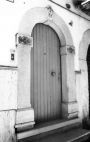Fig. 20 Via Sant'Antonio da Padova 3. Portale ad arco a tutto sesto con stemma in chiave d'arco di forma pentagonale decorato con elementi a bassorilievo ed iscrizione; con imposte dei piedritti e basi rimarcate. Particolare: Stemma in chiave d'arco di forma pentagonale con elementi a bassorilievo ed iscrizione su due righe: 'A.V.' (Angelo Villani), '1871'.