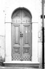 Fig. 43 Via Arimondi 5. Portale ad arco a tutto sesto con imposte dei piedritti e basi rimarcate, con stemma in chiave d'arco di forma pentagonale, contenente una figura floreale ed iscrizione data. Particolare: Stemma in chiave d'arco di forma pentagonale con figura di giglio a bassorilievo e iscrizione data '1937'.